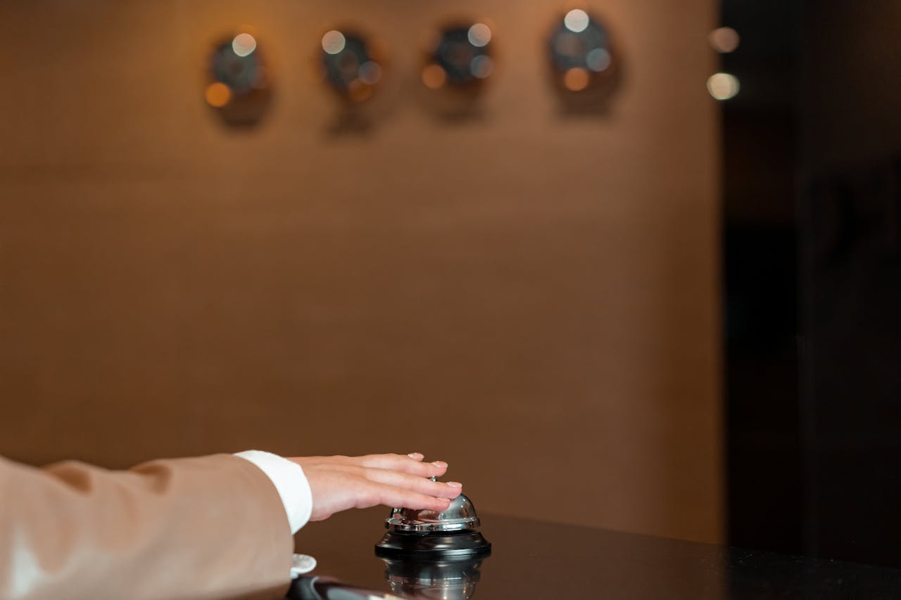 A hand pressing a bell at a hotel reception, symbolizing service and hospitality.